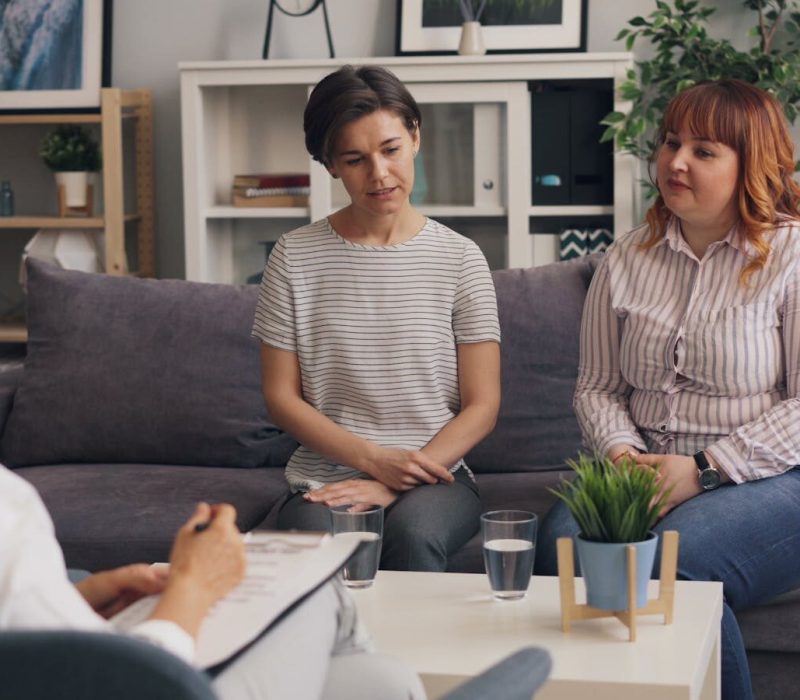 Therapist conducting a session with two clients in a cozy office environment.