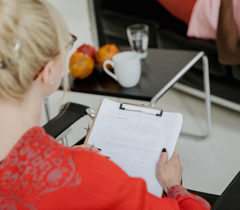 A psychologist takes notes during a therapy session with a client, indoors.